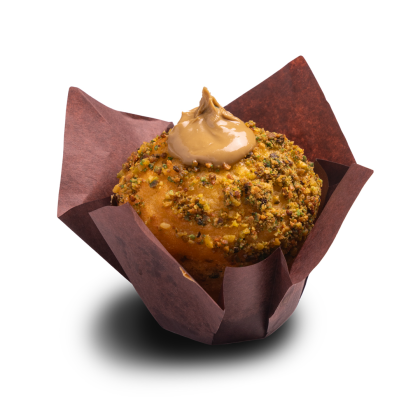 Muffin coated in crushed pistachios, topped with a swirl of caramel frosting, in a brown tulip wrapper.