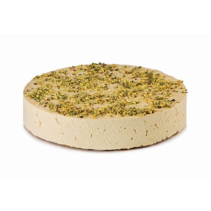 Round disc of pale halva topped with chopped pistachios, showing a dense, crumbly texture on a white background.