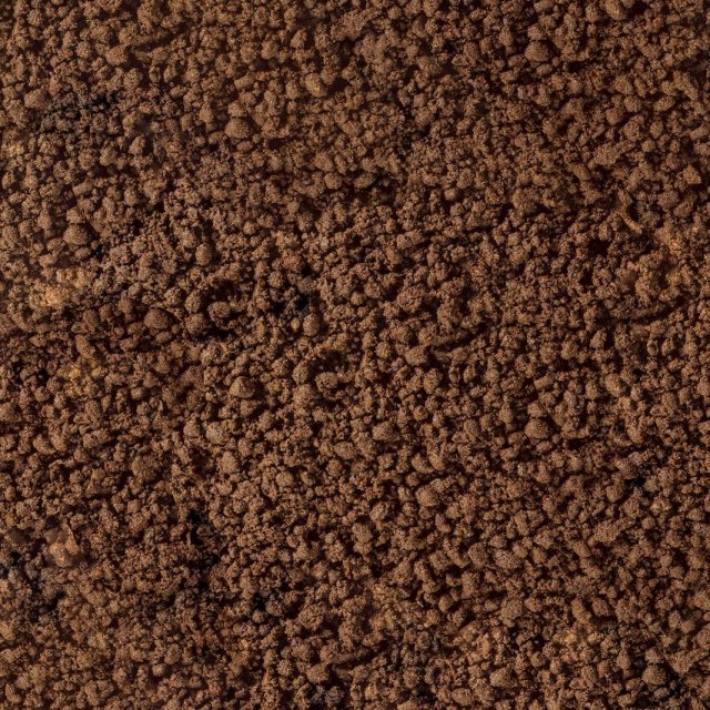 Close-up of crumbly brown soil or coffee grounds with a coarse, granular texture filling the frame.