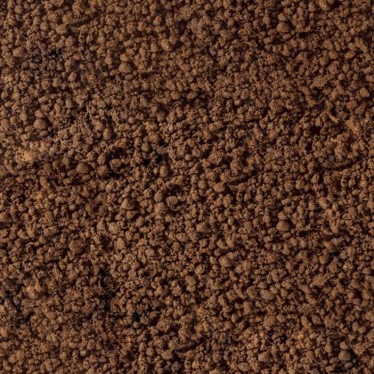 Close-up of crumbly brown soil or coffee grounds with a coarse, granular texture filling the frame.
