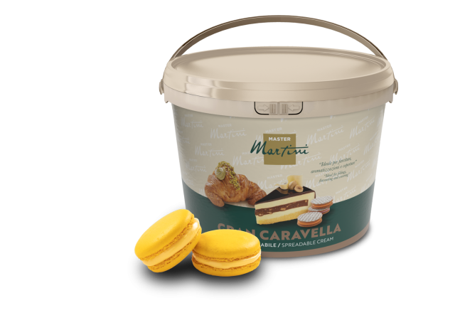 A tan bucket of Master Martini Gran Caravella spreadable cream beside two yellow macarons and a filled pastry.