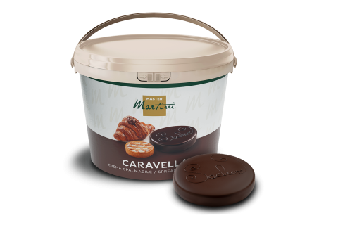 A large white bucket labeled "Master Martini Caravella" spreadable cream, beside a round dark chocolate disc with emb...