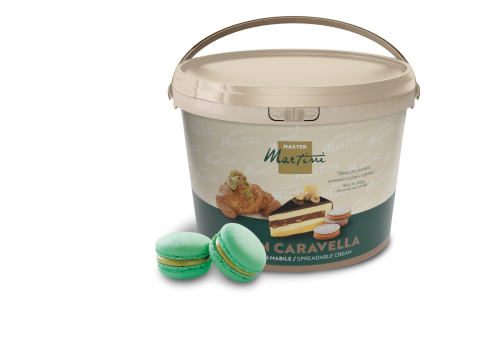 Beige tub of Master Martini spreadable cream with pastry images, next to two green pistachio macarons.