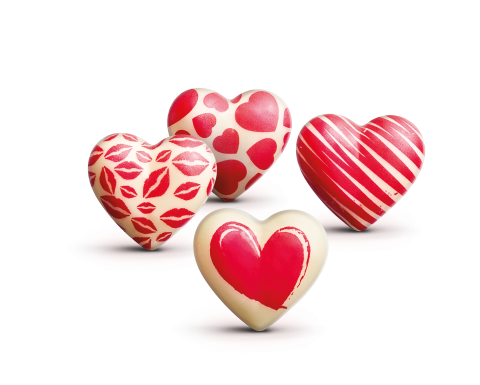 Four white heart-shaped chocolates decorated with red lip prints, hearts, stripes, and a painted heart pattern.