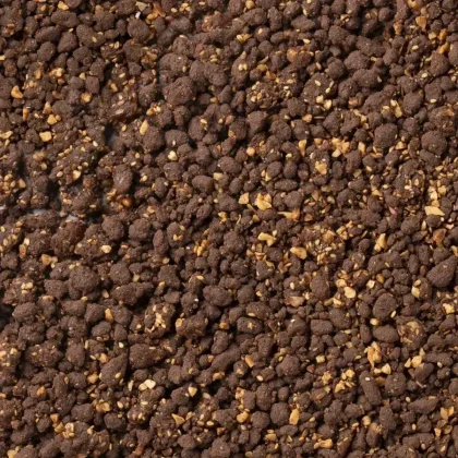Close-up of a crumbly dark brown mixture with visible chopped nuts, resembling a chocolate crumble or granola texture.