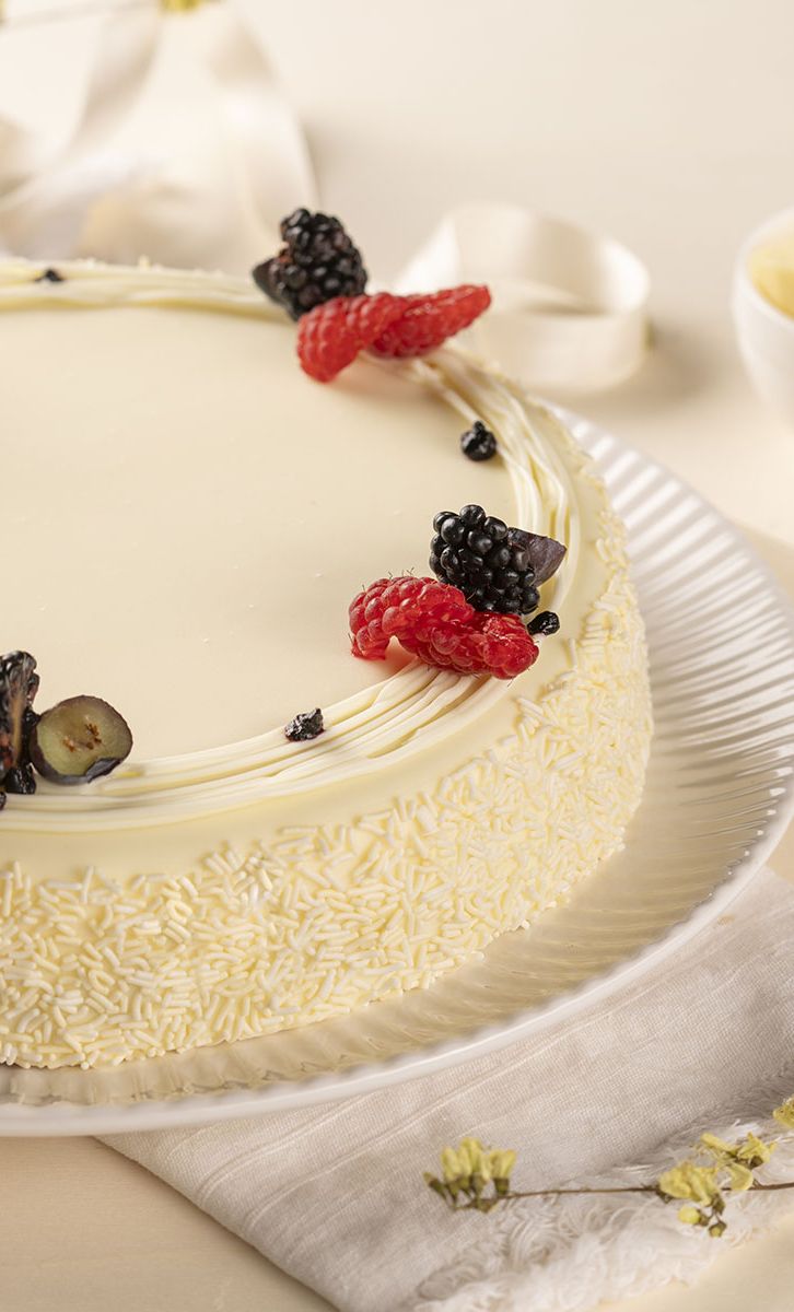 White-frosted cake with raspberries and blackberries, coated in white chocolate shavings on a plate.