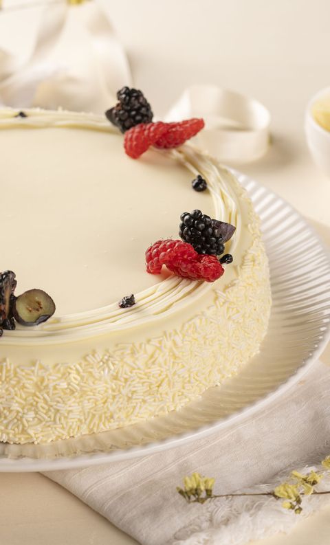 White-frosted cake with raspberries and blackberries, coated in white chocolate shavings on a plate.