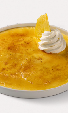Caramelized custard dessert in a white dish topped with a swirl of whipped cream and pineapple wedge.