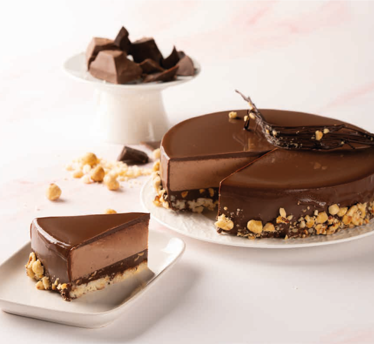 Glossy chocolate mousse cake with crunchy hazelnut base, one slice cut and plated, chocolate shards on top.