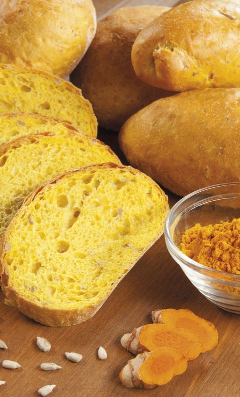Sliced turmeric bread loaves with yellow crumb, whole loaves, a bowl of turmeric powder, sunflower seeds, and fresh t...
