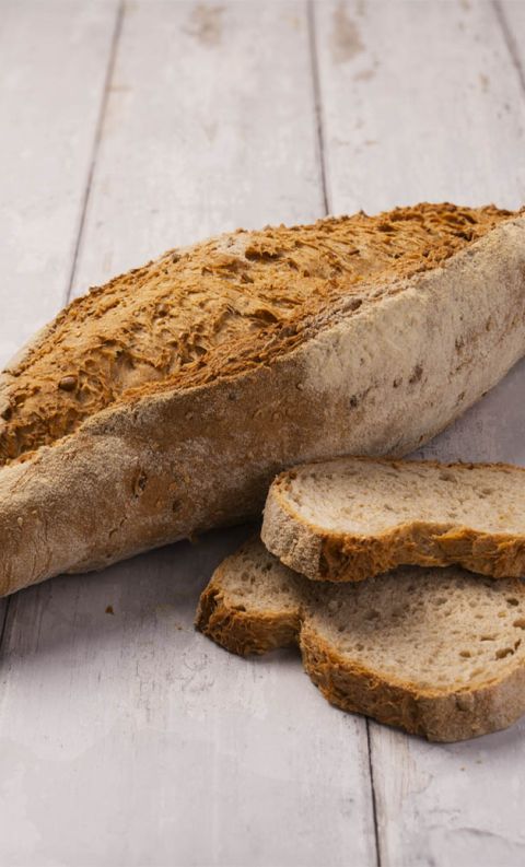 An oblong artisan loaf with a floured, cracked crust beside three cut slices on a whitewashed wooden surface.