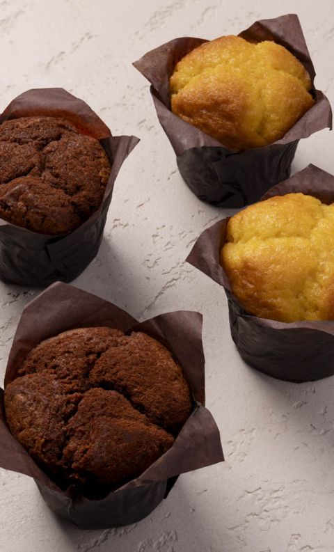 Two chocolate and two vanilla muffins wrapped in brown paper liners, arranged on a textured white surface.