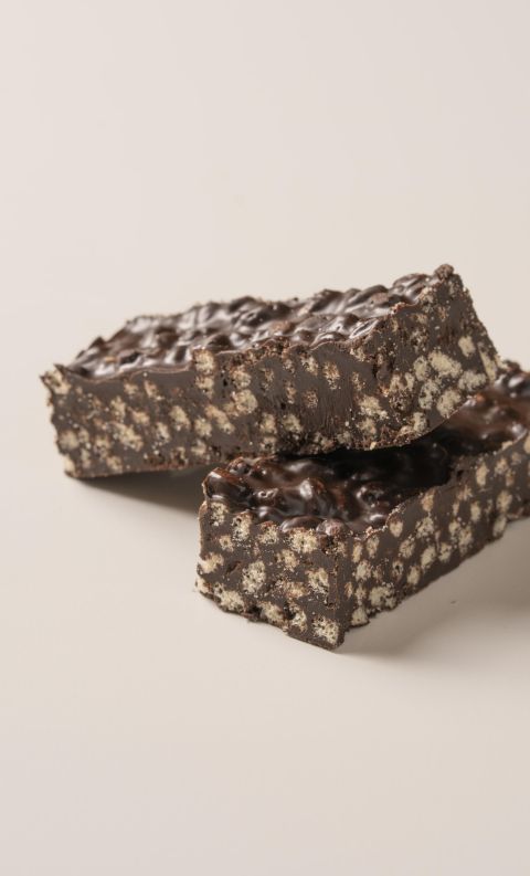 Two chocolate crispy bars stacked on a beige surface, revealing a gooey chocolate filling between crunchy textured la...
