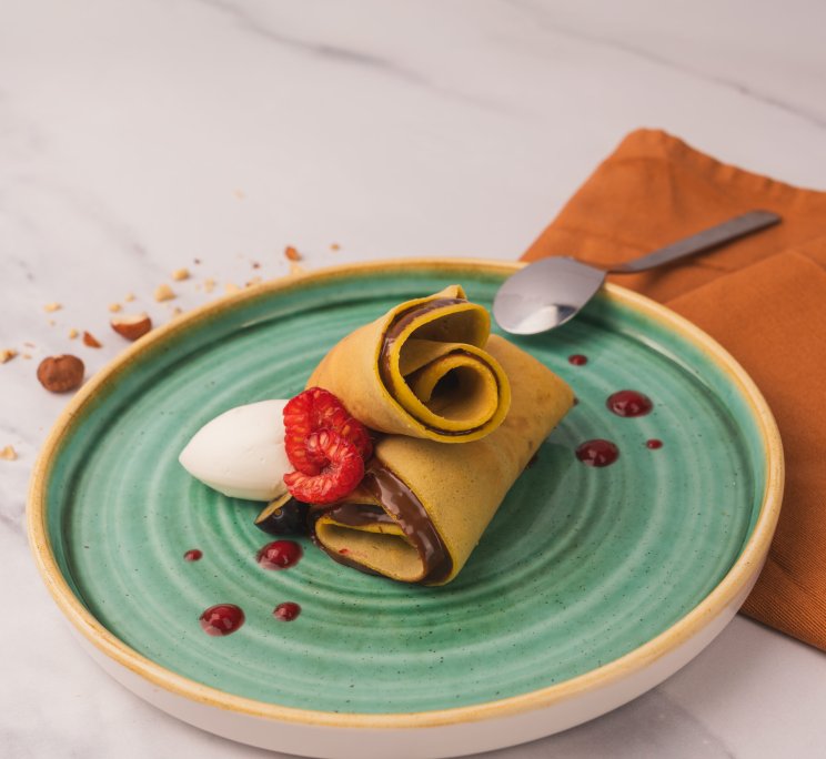 Chocolate-filled crepe rolled and garnished with a fresh raspberry and vanilla ice cream on a teal ceramic plate.