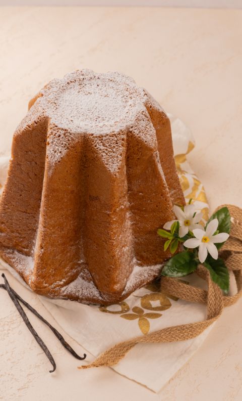 Star-shaped pandoro cake dusted with powdered sugar, garnished with vanilla beans, white flowers, and a burlap ribbon.