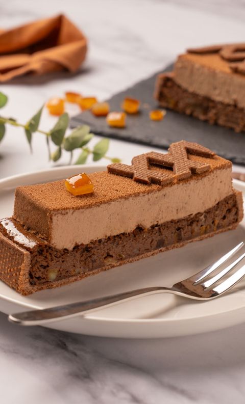 A rectangular chocolate mousse cake slice with nutty crumb base, topped with amber gelée and a chocolate garnish, ser...