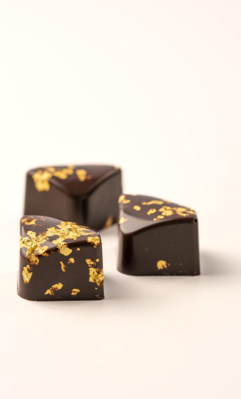 Three dark chocolate truffles with gold leaf flecks on top, arranged on a white background.
