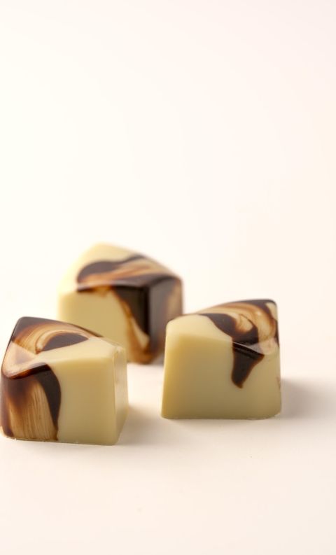 Three cube-shaped white chocolate candies with dark chocolate marbled swirls on a white background.