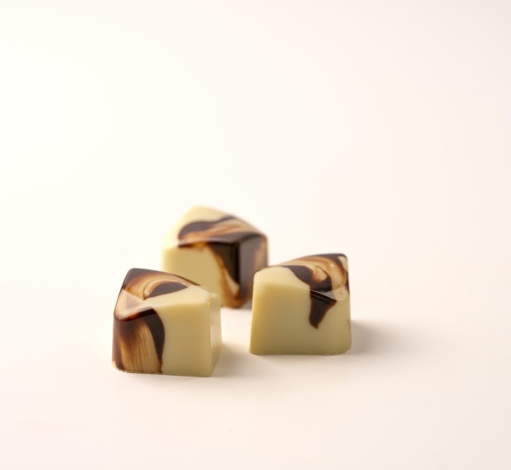 Three cube-shaped white chocolate candies with dark chocolate marbled swirls on a white background.