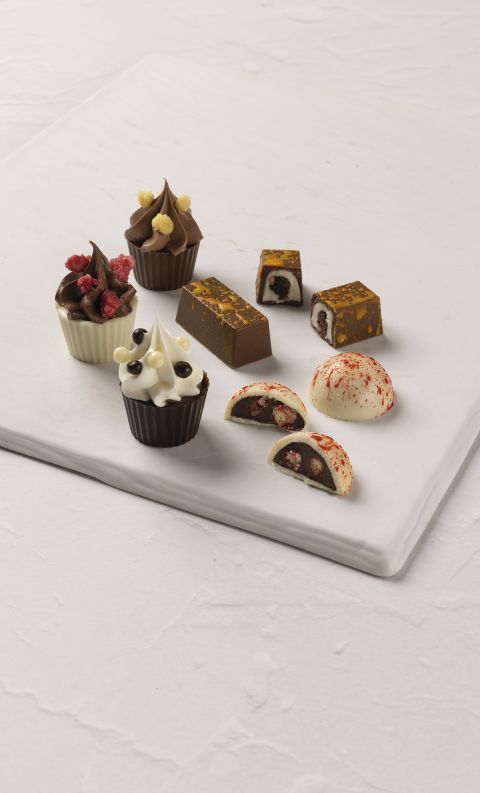 An assortment of gourmet chocolates, including cream-topped cups and filled bonbons, on a white marble slab.