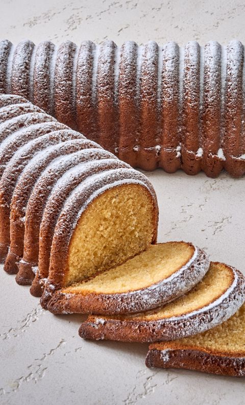 Ridged pound cake with browned, ribbed crust dusted in powdered sugar, partly sliced with three slices fanned in front.